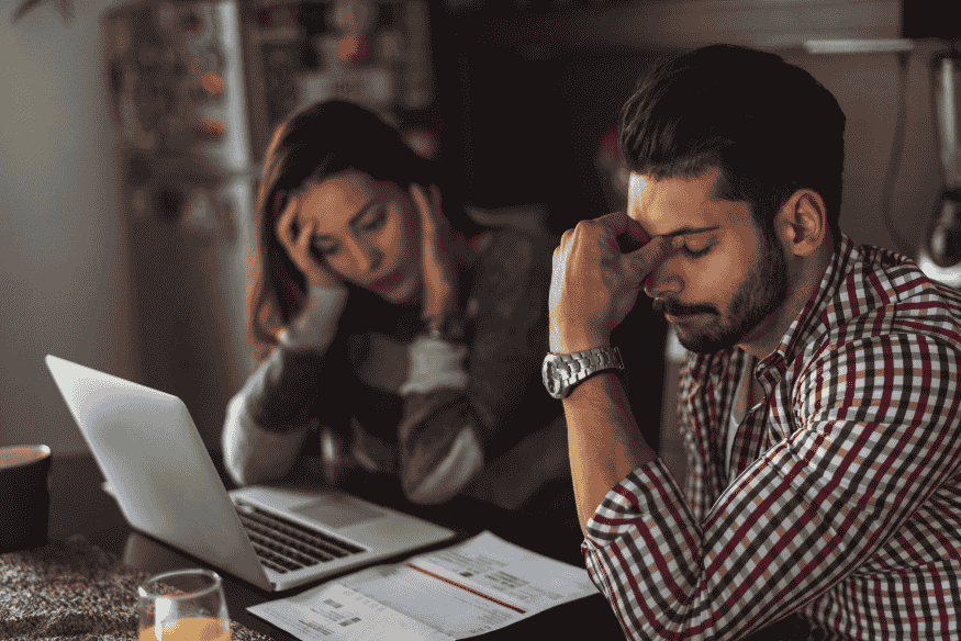 Casal preocupado com as finanças, analisando documentos e laptop, simbolizando o impacto da renegociação de dívidas no score de crédito.
