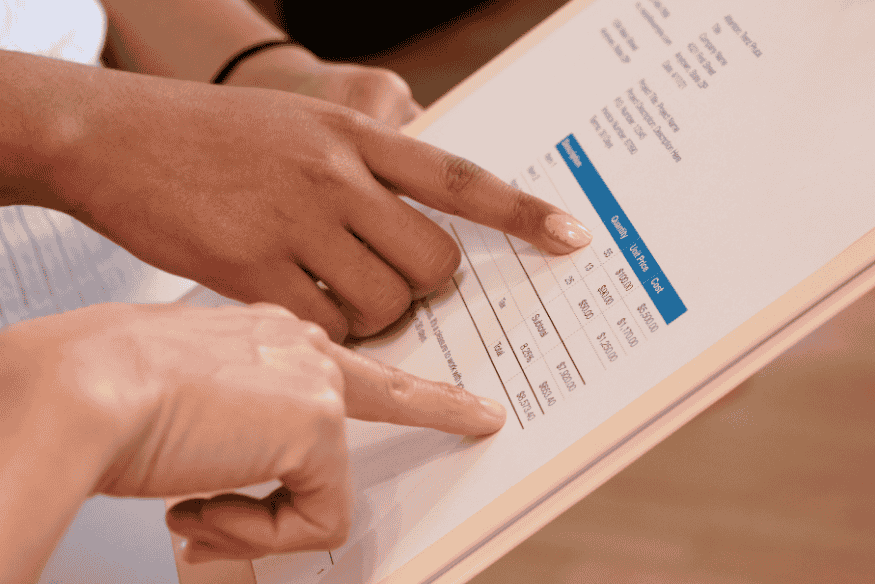 Mãos apontando para documento financeiro com valores e tabelas, simbolizando a importância da carta de quitação como prova do pagamento integral da dívida.