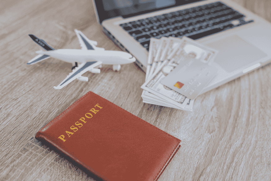 Passaporte, cartão de crédito e dinheiro ao lado de laptop representando vantagens de cashback e milhas em viagens