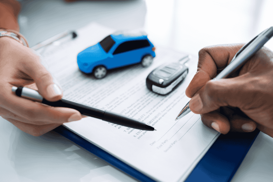 Pessoa assinando contrato de financiamento de carro, com miniatura de automóvel e chave sobre o documento, simbolizando empréstimo para compra imediata.