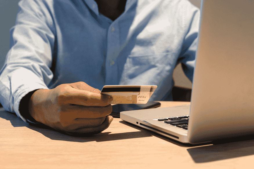 Pessoa segurando um cartão de crédito em frente a um laptop, simbolizando a importância do uso consciente do crédito para construir um bom histórico.