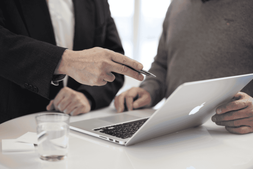 Pessoas discutindo sobre informações financeiras em um laptop, simbolizando a análise de consultas ao CPF e seu impacto no score de crédito.