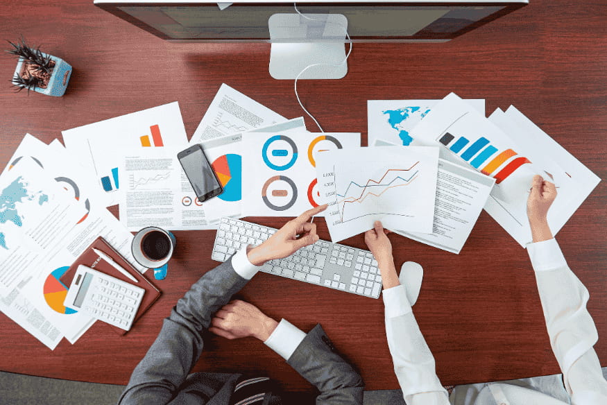 Duas pessoas analisando gráficos e documentos financeiros, simbolizando o processo de revisão e correção de erros no relatório de crédito.