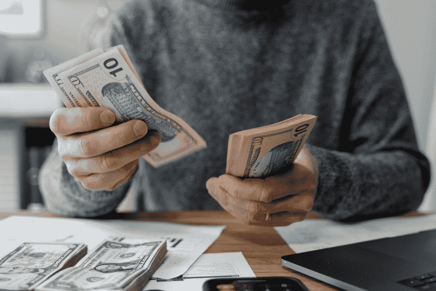 Pessoa contando dinheiro em notas de dólar sobre mesa com documentos, representando o controle financeiro proporcionado pelas parcelas fixas em contratos de crédito.