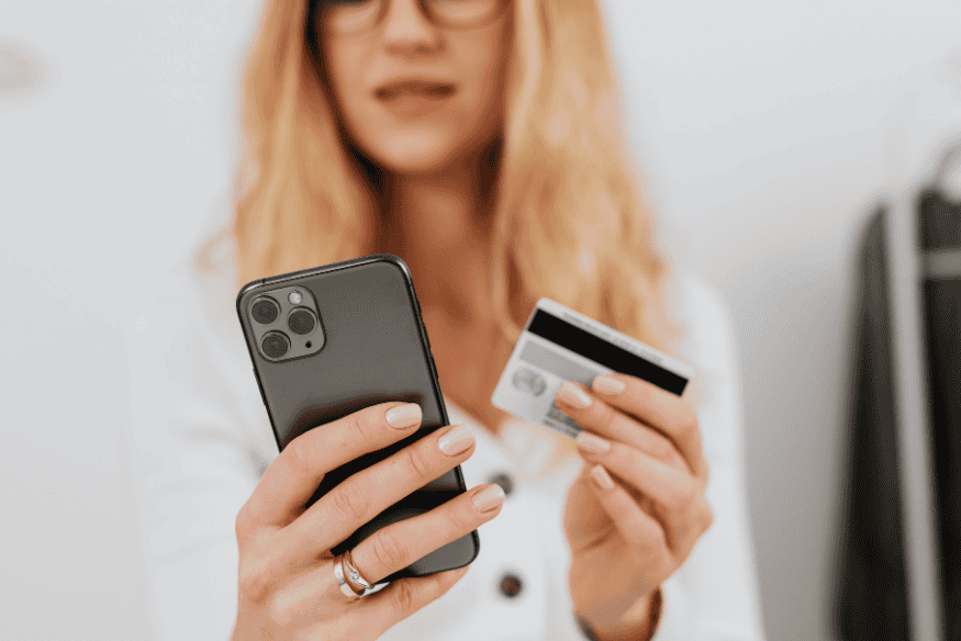 Pessoa usando celular e cartão de crédito para fazer compra online, exemplo de pagamento recorrente em serviços digitais