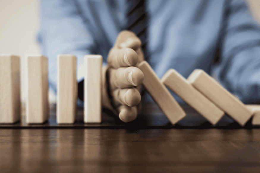 Homem interrompendo a queda de peças de dominó, simbolizando a interrupção e a suspensão do prazo prescricional das dívidas no Brasil.