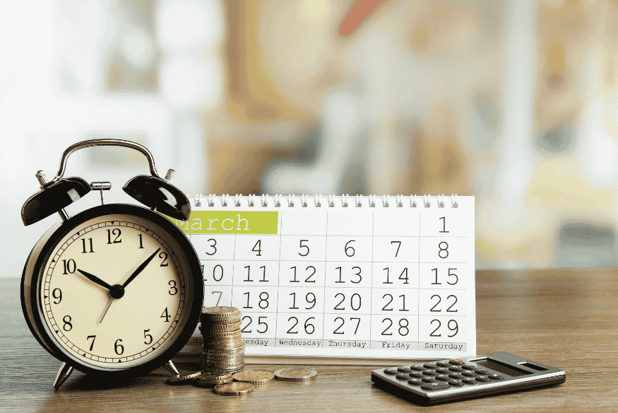 Relógio, calendário, moedas empilhadas e calculadora sobre a mesa, simbolizando a importância da pontualidade nos pagamentos para fortalecer o score de crédito de MEIs e autônomos.