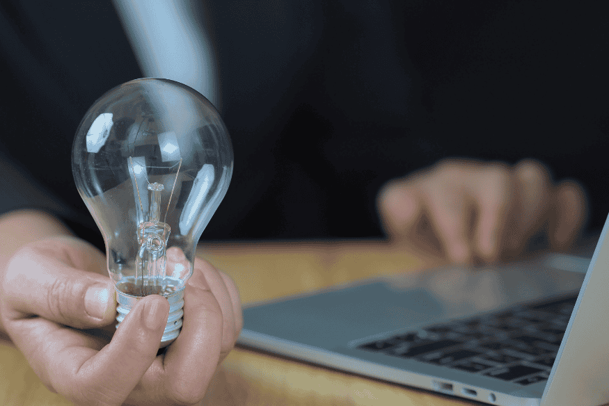 Empresário segurando uma lâmpada ao lado de um notebook, simbolizando ideias estratégicas para fortalecer o score de crédito de MEIs e autônomos.