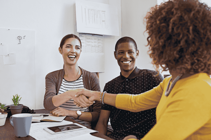 Pessoas em reunião sorridentes, selando acordo com aperto de mãos, simbolizando a negociação de dívidas com credores utilizando renda extra como o 13º salário.