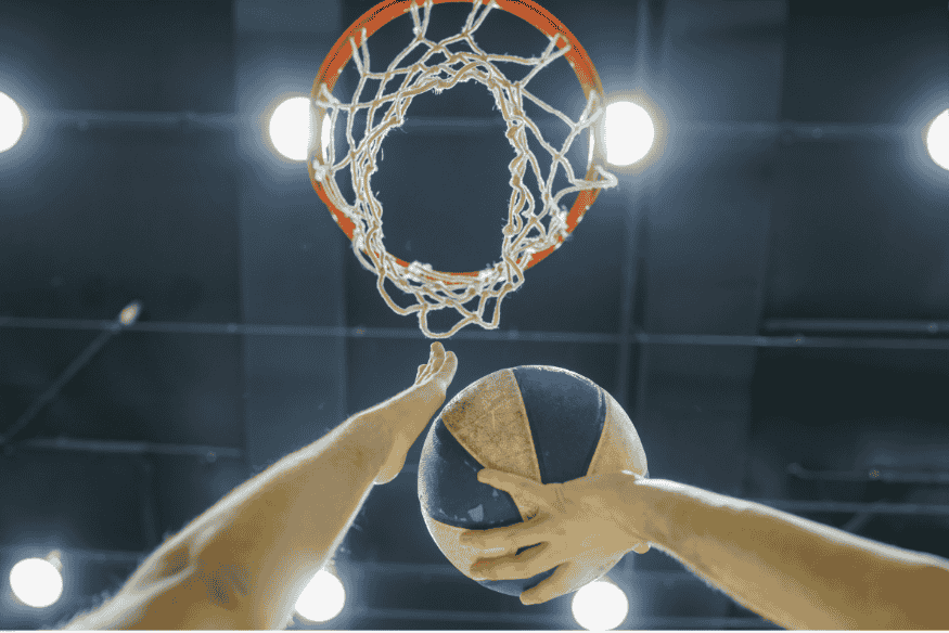 Mãos segurando bola oficial de basquete 3x3 em direção à cesta durante uma enterrada.