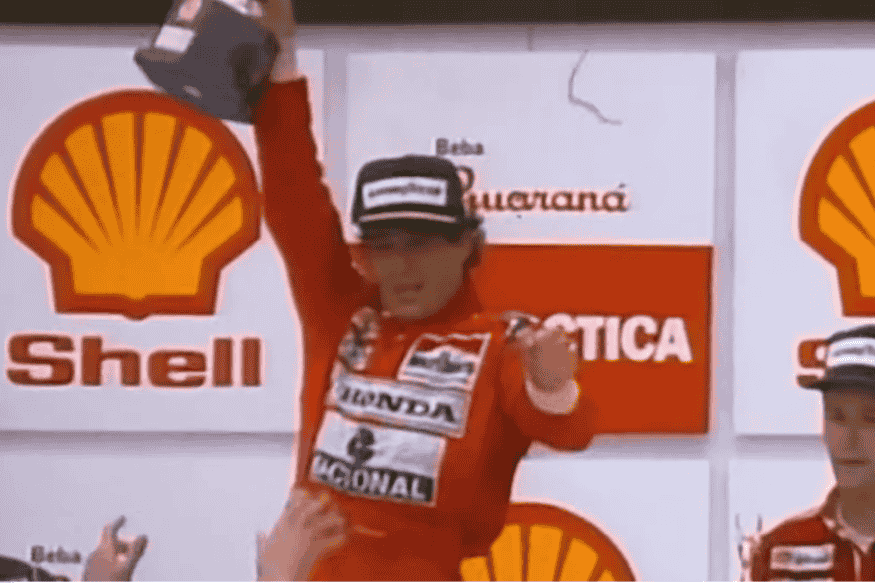 Ayrton Senna no pódio comemorando vitória com troféu em mãos e uniforme da McLaren.