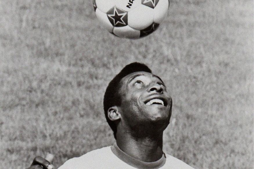 Pelé sorridente olhando para cima enquanto faz embaixadinha com bola de futebol.