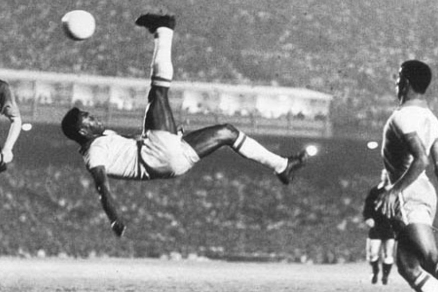 Pelé realizando uma bicicleta em jogo noturno, com outros jogadores ao fundo.
