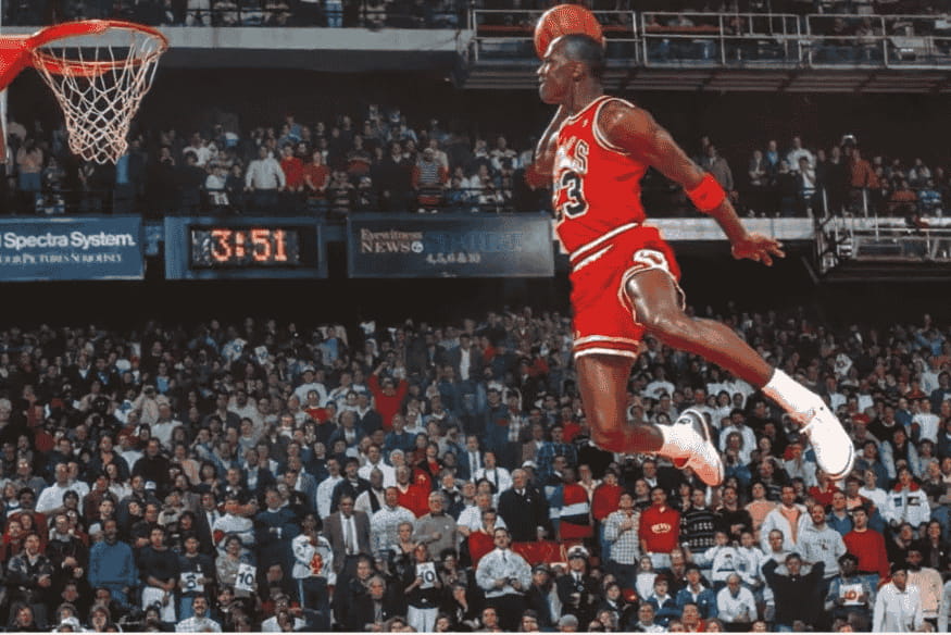 Michael Jordan realizando enterrada durante partida diante de arquibancada lotada.