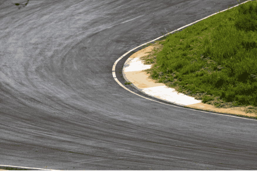 Curva fechada de um circuito de rua com área de escape gramada e pista marcada.
