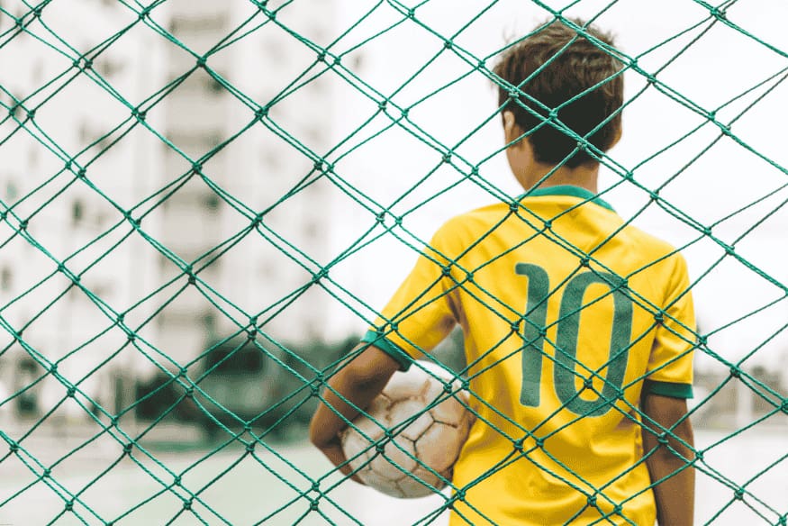 Garoto com camisa número 10 segurando bola de futebol em quadra cercada por rede.