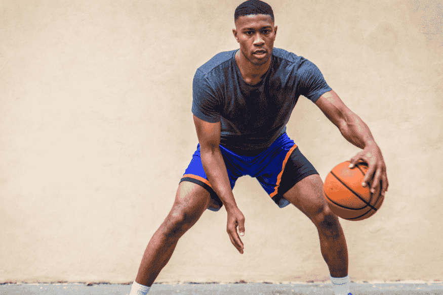 Jovem jogador de basquete driblando com intensidade durante treino em ambiente simples.