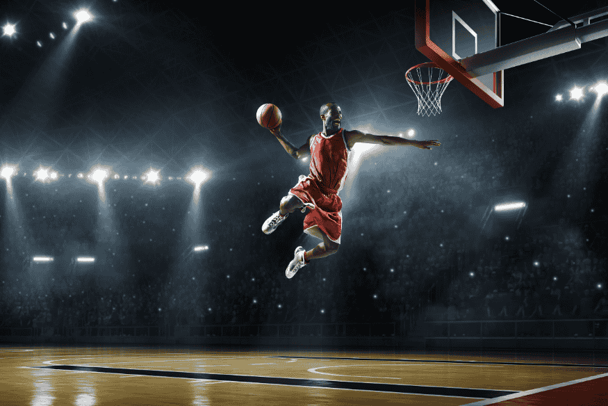 Jogador de basquete voa em direção à cesta durante enterrada em quadra profissional com luzes intensas.