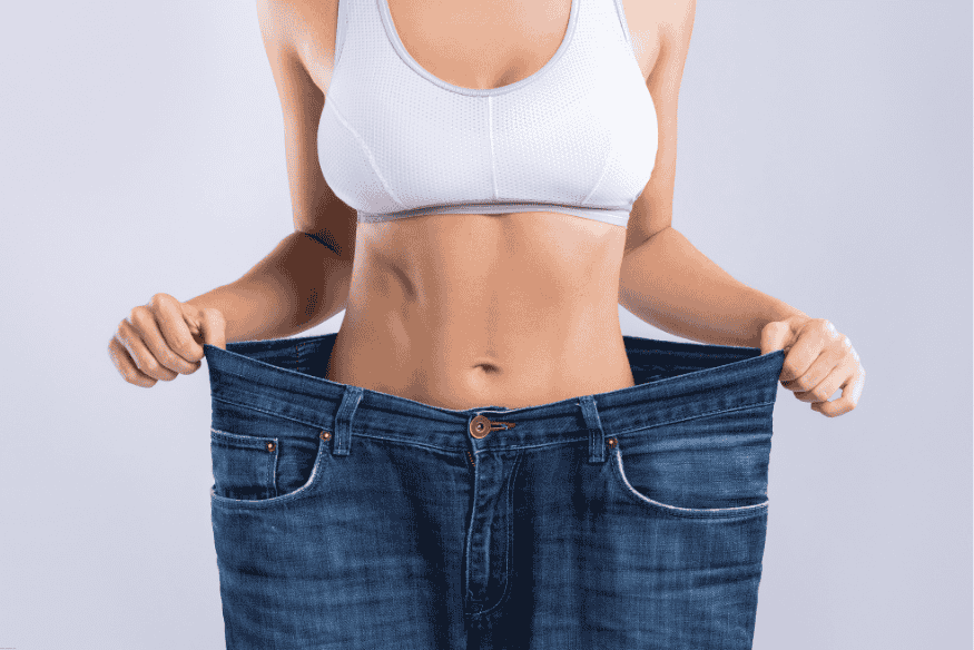 Mulher mostrando calça jeans larga após perda significativa de peso.