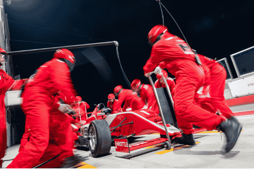 Equipe de pit stop trabalhando em conjunto em carro de Fórmula 1 durante corrida noturna.