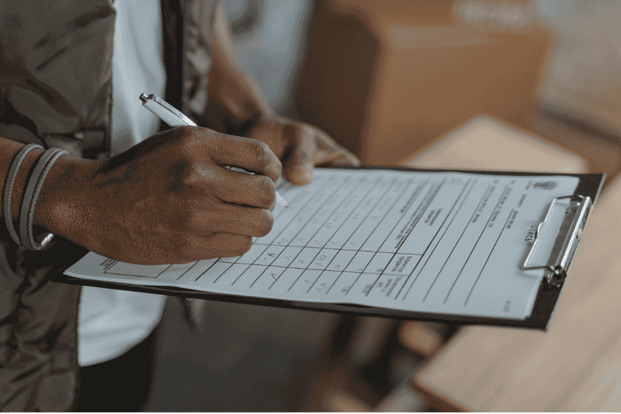 Pessoa preenchendo formulário técnico com prancheta em ambiente de trabalho.