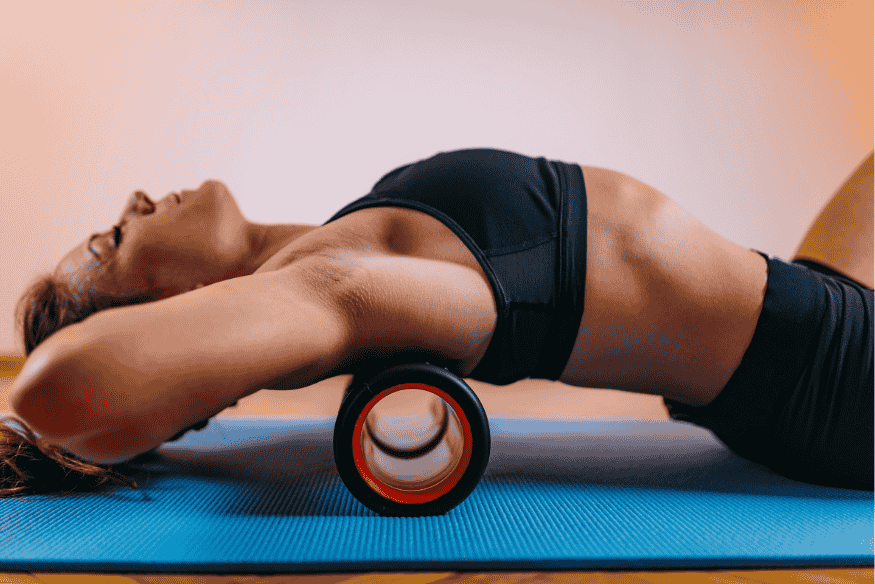 Mulher deitada com o foam roller sob a parte superior das costas realizando liberação miofascial.