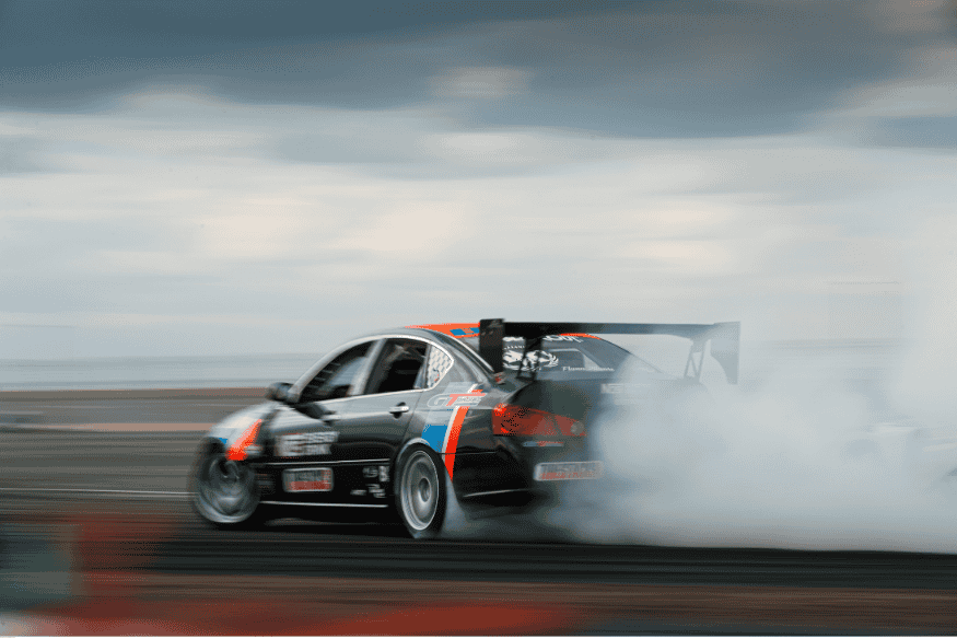 Carro de corrida preto derrapando com fumaça saindo dos pneus em pista de corrida.
