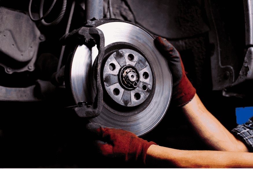 Técnico instalando disco de freio em carro com sistema de suspensão exposto.