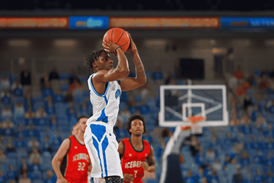 Jogador em uniforme branco realiza arremesso de basquete com técnica apurada em quadra profissional.