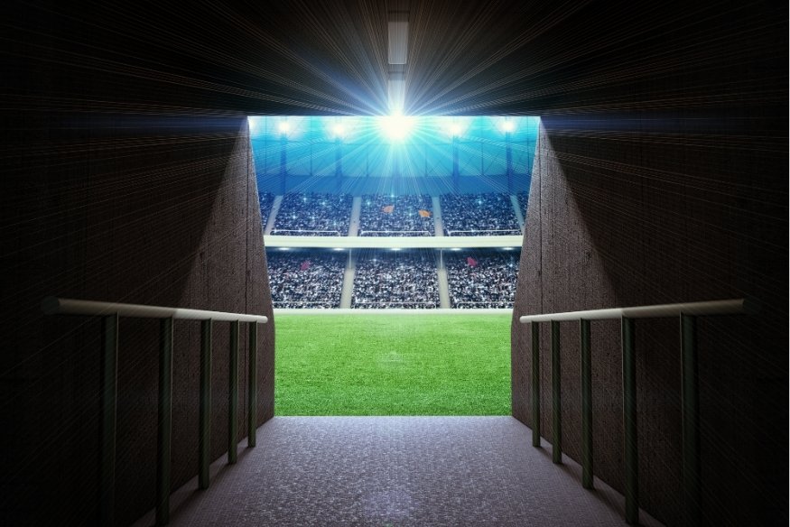 Entrada do túnel de estádio de futebol levando ao campo iluminado durante partida do Brasileirão, representando a atmosfera vibrante do campeonato nacional.
