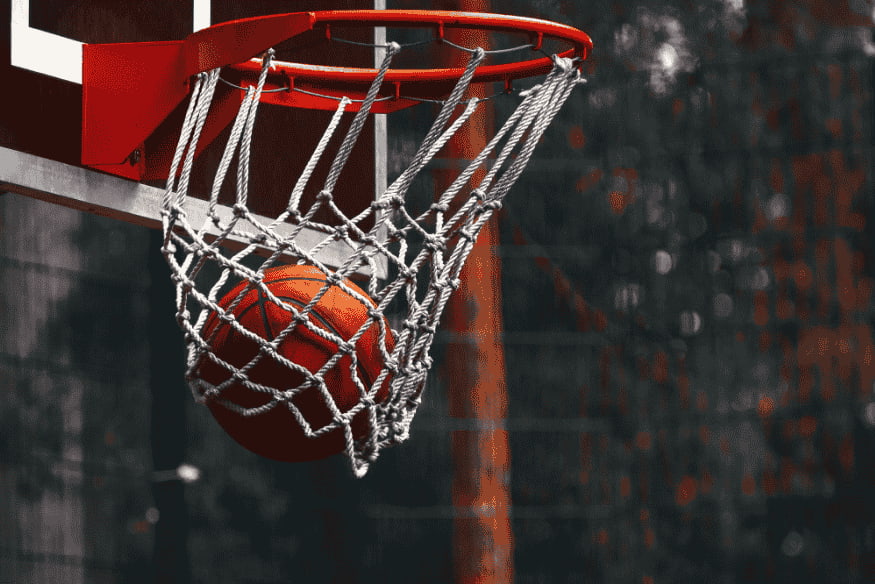 Bola de basquete atravessando a rede da cesta em quadra externa, simbolizando pontuação.