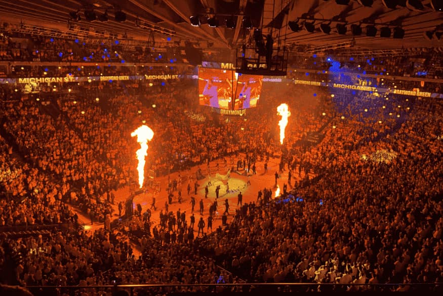 Arena lotada durante evento da NBA com efeitos de fogo e iluminação antes de uma partida.