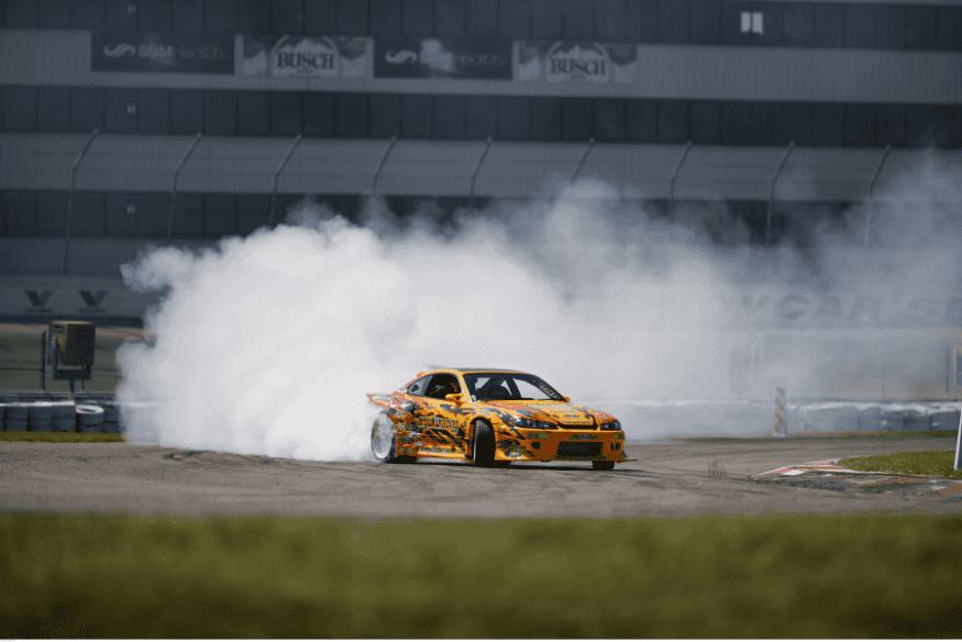 Carro de corrida amarelo realizando manobra de drift em pista de asfalto com fumaça.