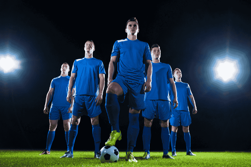 Time de futebol posicionado em campo sob refletores à noite.