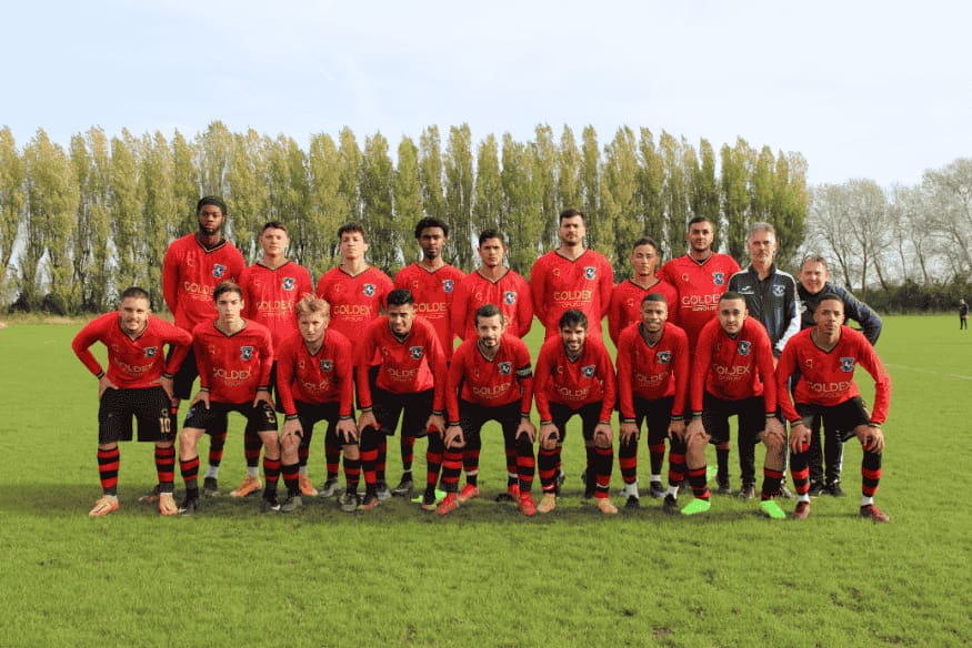 Equipe de futebol posando para foto oficial em campo gramado.