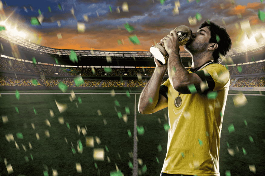 Jogador de futebol com uniforme amarelo beija troféu em campo, celebrando título.