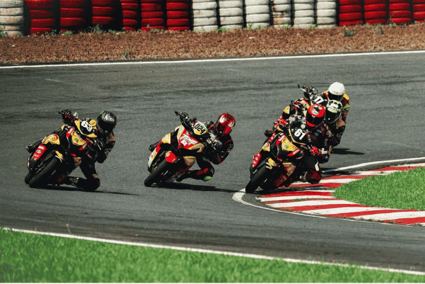 Grupo de pilotos disputando curva em pista de corrida de MotoGP, com motos esportivas em alta velocidade.