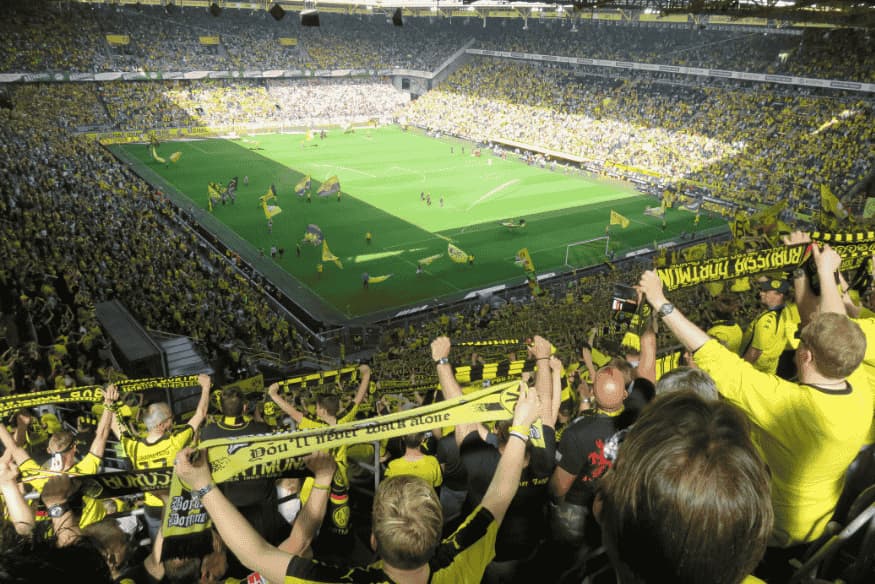 Torcida lota as arquibancadas de um estádio durante partida decisiva de futebol.