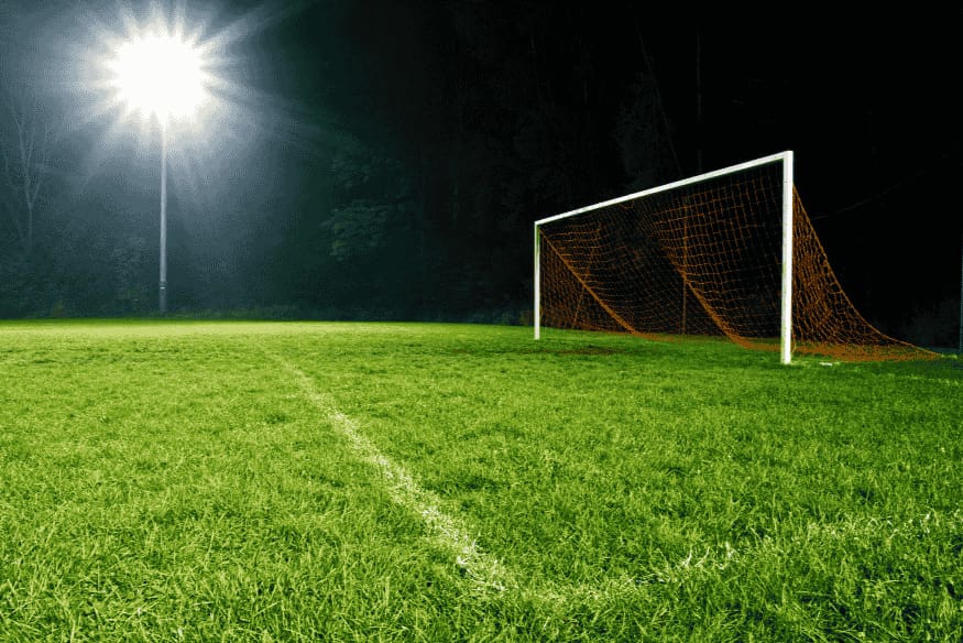 Gol de futebol iluminado por refletores à noite, com campo vazio.