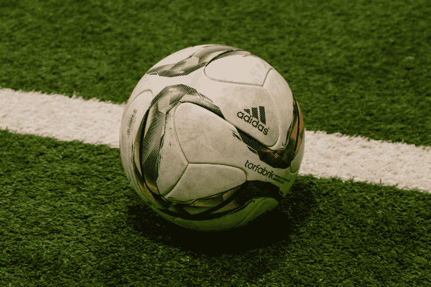Bola de futebol Adidas sobre linha branca em campo de grama artificial.
