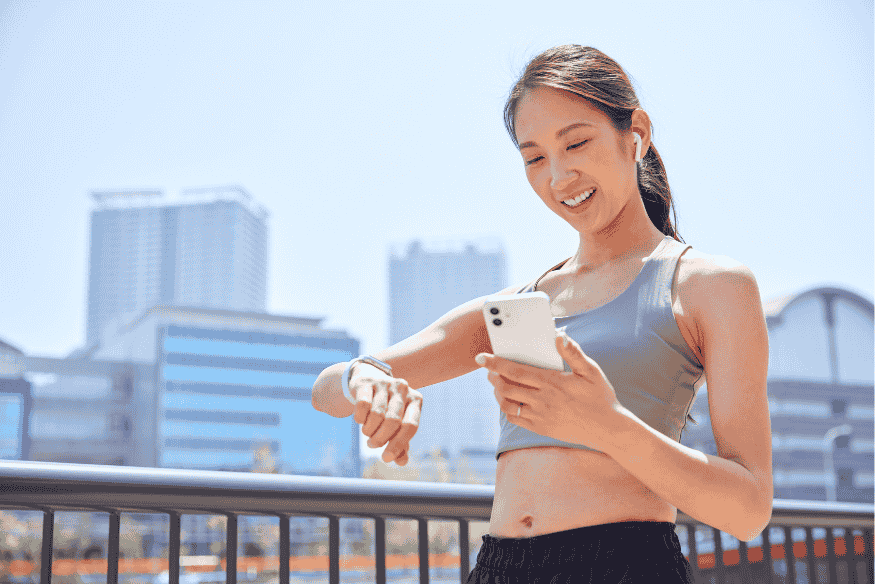 Corredora consultando app de corrida no celular e no relógio inteligente
