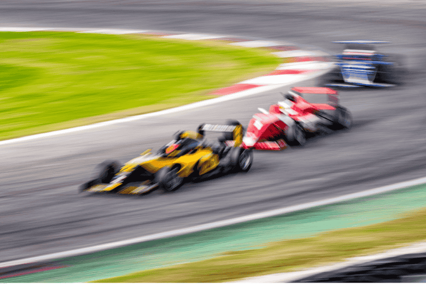 Carros de Fórmula 1 em movimento rápido durante curva, com destaque para manobra de ultrapassagem.