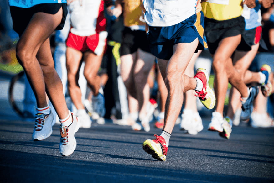 Detalhe dos pés de corredores em movimento durante uma meia maratona, ilustrando ritmo e cadência.