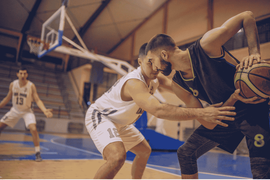 Jogador com bola utiliza bloqueio de companheiro para driblar marcação em quadra coberta.