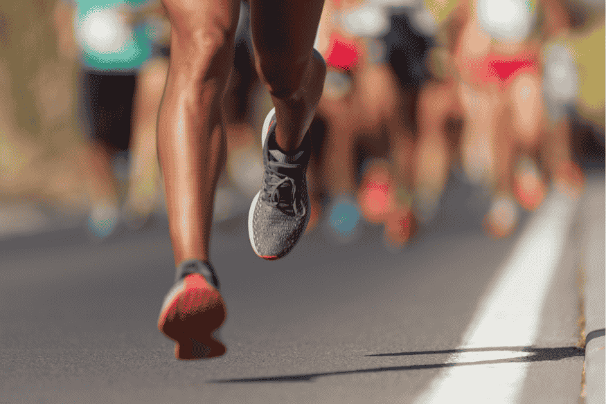 Corredor de rua em movimento com foco nos tênis de corrida, em meio a outros participantes.