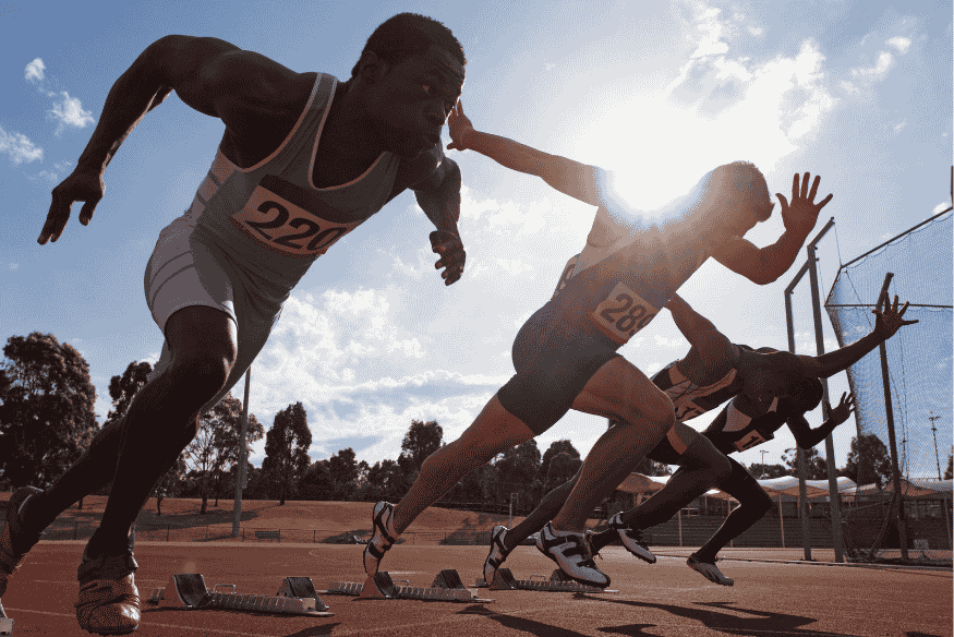 Corredores iniciando uma prova de atletismo em pista ao ar livre, com explosão de velocidade.