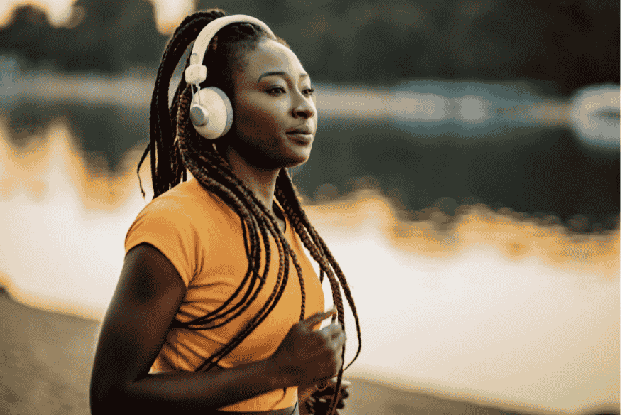 Corredora com tranças e camiseta laranja corre ouvindo música com fones grandes.