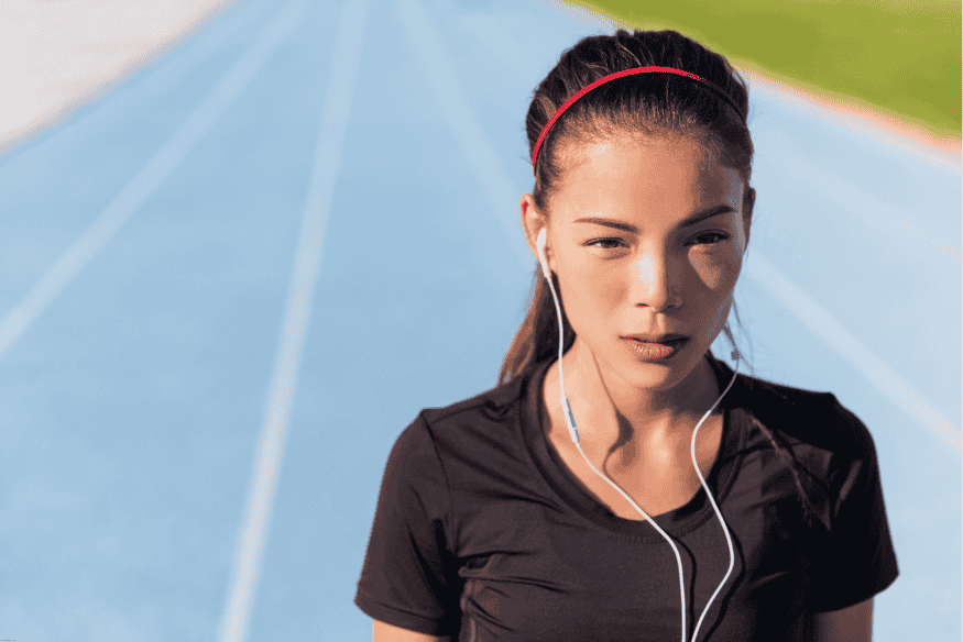 Mulher com fone de ouvido e faixa vermelha na cabeça, pronta para correr em pista azul.