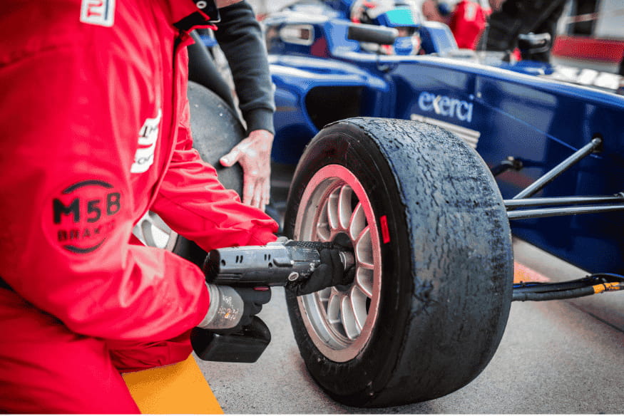 Membro da equipe de box da Fórmula 1 utilizando ferramenta para trocar pneu durante pit stop.