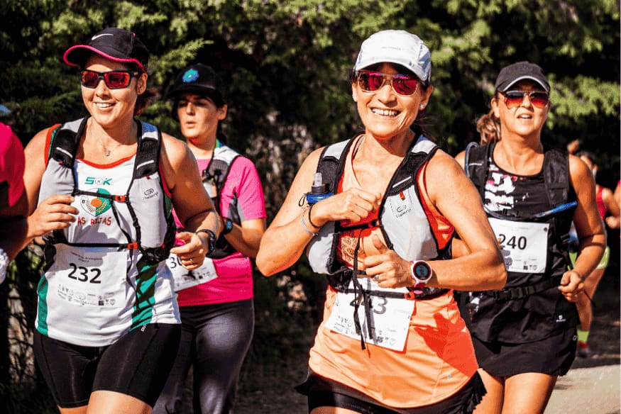Mulheres sorrindo e correndo com coletes de hidratação durante uma corrida de rua no Brasil